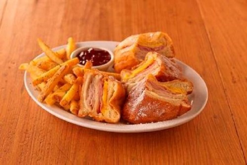 A plate of crispy fries and a sandwich filled with ham and cheese, served with a side of dipping sauce.