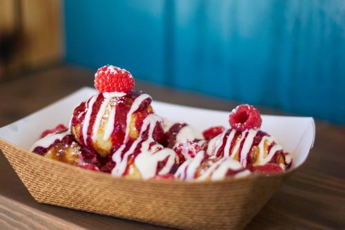 A tray of dessert balls drizzled with white icing and raspberry sauce, topped with fresh raspberries.