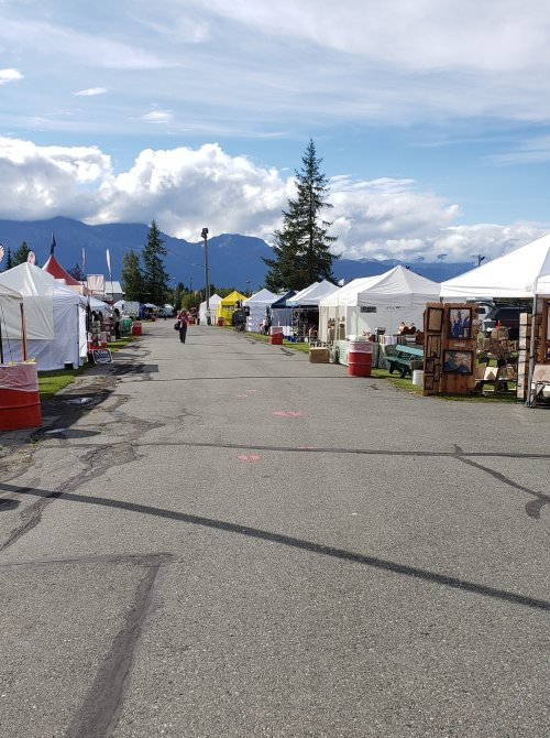 A wide view of a market street lined with vendor tents, mountains in the background, and a cloudy sky above.
