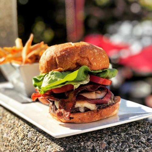 A juicy burger with bacon, cheese, lettuce, and tomato, served with a side of crispy fries on a white plate.