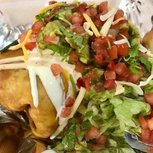 A close-up of a loaded taco with guacamole, diced tomatoes, lettuce, cheese, and sour cream on a crispy shell.
