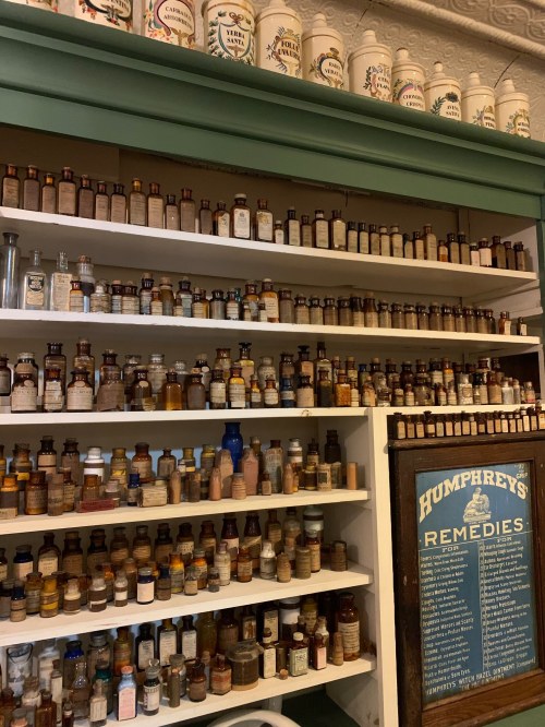 A wooden shelf filled with numerous vintage medicine bottles and a sign reading "Humphrey's Remedies."