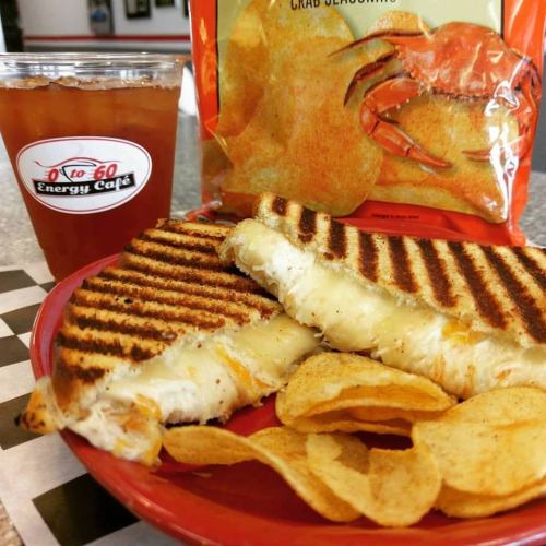 A grilled cheese sandwich with chips and a drink on a red checkered plate, with a bag of crab chips in the background.
