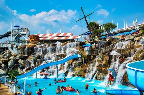 A vibrant water park scene featuring a waterfall, water slides, and people enjoying the pool under a blue sky.