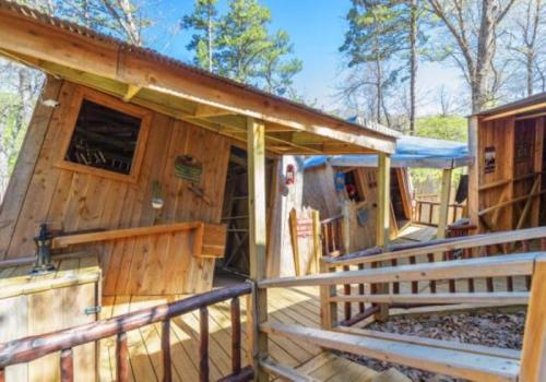 A unique wooden cabin with a slanted roof, surrounded by trees and featuring a wooden deck and railings.