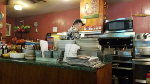A chef in a colorful shirt prepares food in a cozy restaurant kitchen, surrounded by plates and kitchen equipment.