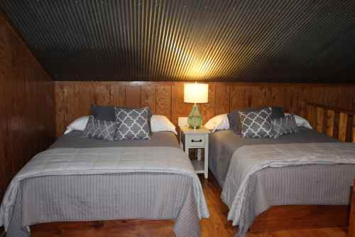 Cozy attic bedroom with two beds, gray bedding, a nightstand, and a lamp against wooden walls.