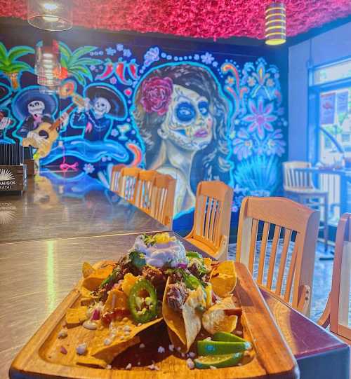 A vibrant restaurant scene featuring a colorful mural and a plate of nachos topped with various ingredients.