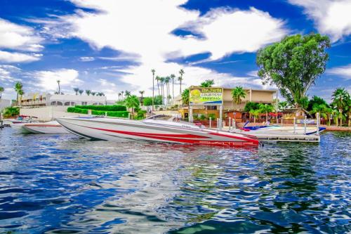 A sleek red and white boat docked on calm water, with palm trees and a building in the background under a blue sky.