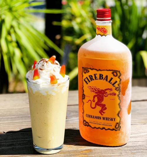 A glass of creamy drink topped with whipped cream and candy, next to a bottle of Fireball Cinnamon Whisky.