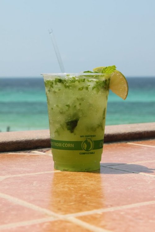 A refreshing green drink with mint and a lime wedge, set against a beach and ocean backdrop.