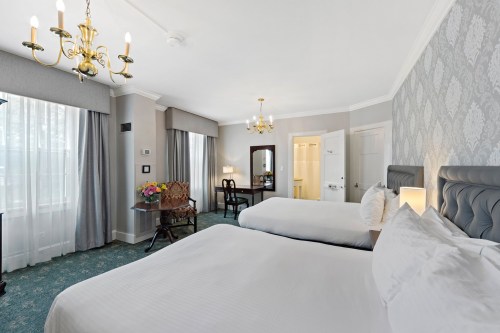 A cozy hotel room featuring two beds, a desk, and elegant decor with large windows and soft lighting.