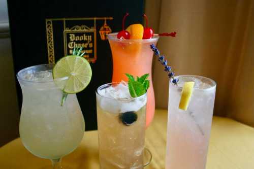 Four colorful cocktails with garnishes, served in various glasses, against a dark menu backdrop.