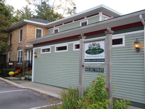 A green building with a sign reading "Hidden Garden" and a welcoming entrance, surrounded by plants and flowers.