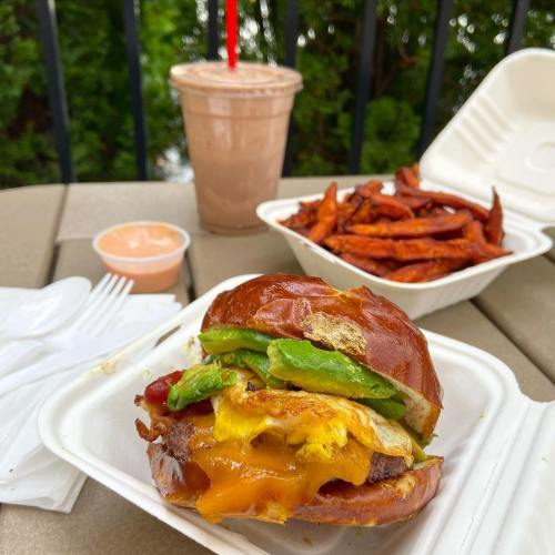 A delicious burger with cheese, lettuce, and sauce, accompanied by sweet potato fries and a chocolate milkshake.
