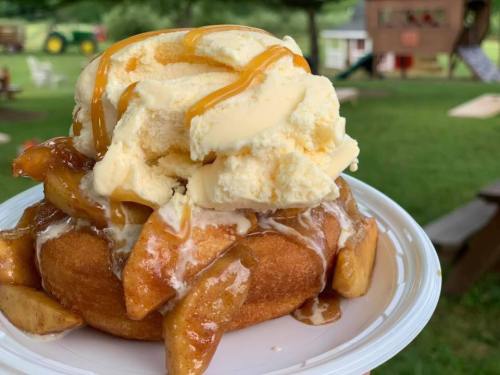 A warm donut topped with caramelized apples, vanilla ice cream, and drizzled with caramel sauce on a white plate.