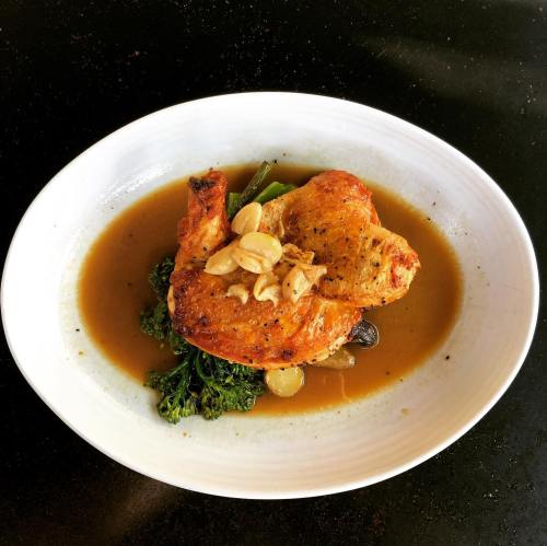 A plate of roasted chicken with almonds, served on a bed of greens and a savory sauce.