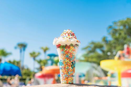 A colorful ice cream sundae topped with whipped cream and sprinkles, set against a sunny poolside background.