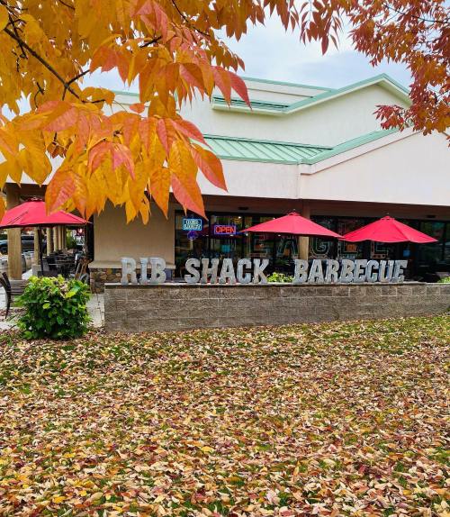 A barbecue restaurant with a sign reading "Rib Shack Barbecue," surrounded by autumn leaves and red umbrellas.