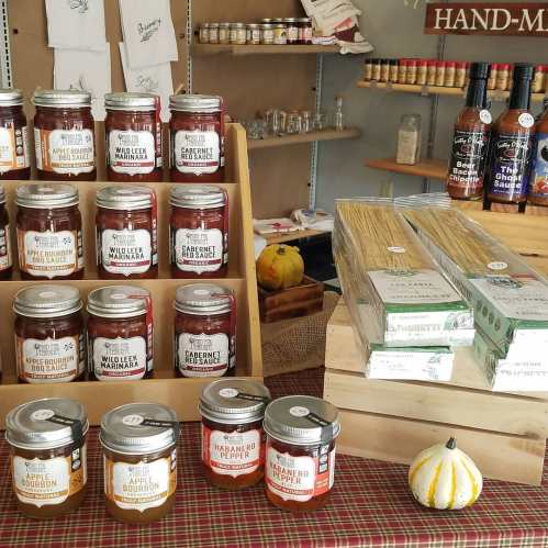 A display of jars and packages on wooden shelves, featuring various sauces, spices, and pasta in a cozy shop setting.