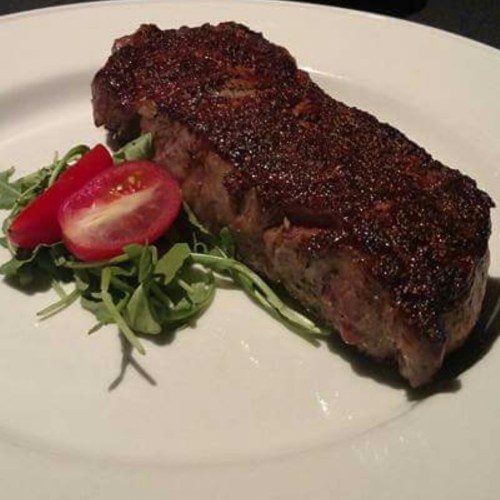 A perfectly cooked steak on a plate, garnished with arugula and cherry tomatoes.
