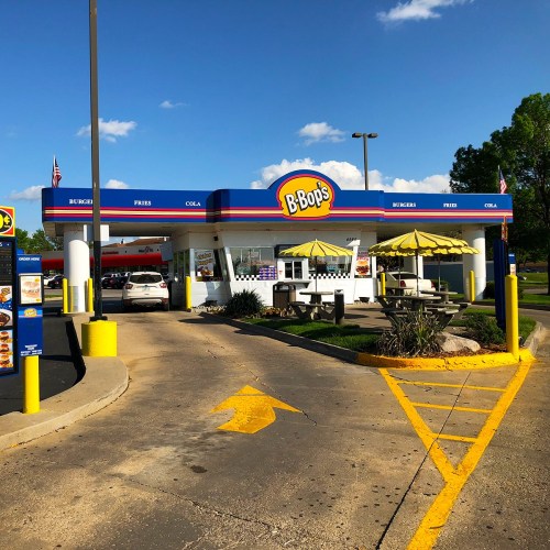 A fast-food restaurant with a colorful sign, outdoor seating, and a drive-thru under a clear blue sky.