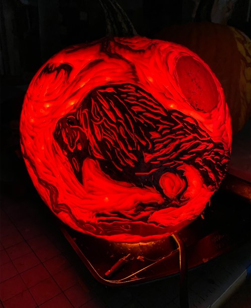 A glowing red pumpkin with intricate carvings, showcasing swirling patterns and a dark, textured design.
