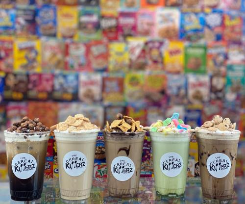Five colorful milkshakes topped with cereal and whipped cream, set against a vibrant background of cereal boxes.
