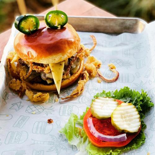 A juicy burger with cheese, jalapeños, and crispy onions, served with a side of lettuce, tomato, and pickles.