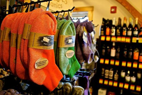 Colorful organic socks hanging on a display, with a shelf of wine bottles in the background.