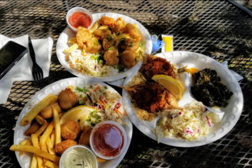 Three plates of fried seafood, coleslaw, fries, and dipping sauces on a table outdoors.