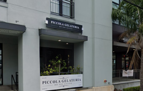 Exterior of Piccola Gelateria, featuring a sign and a small plant in front of a modern building.