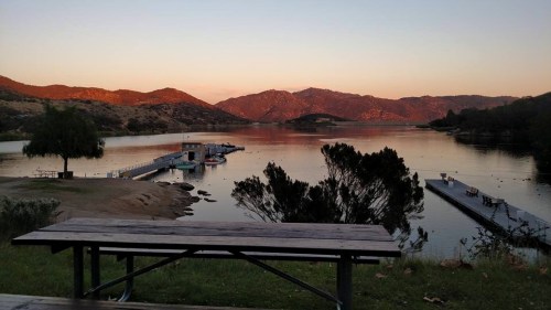 Scenic view of a calm lake at sunset, with mountains in the background and a dock extending into the water.
