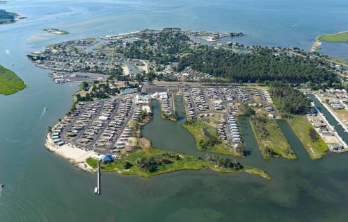 Aerial view of a coastal area with a marina, residential buildings, and waterways surrounded by greenery.