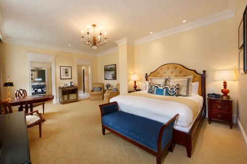 A spacious hotel room featuring a large bed, elegant decor, a seating area, and warm lighting.