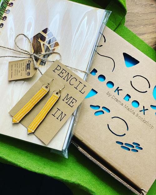 A flat lay of a notebook, earrings, and a box labeled "BOOK BOX" on a green background.