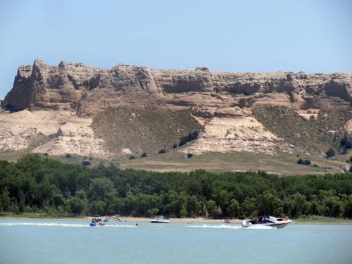 A scenic view of a river with boats, framed by a rocky cliff and lush greenery in the background.