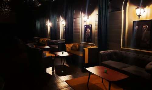 Dimly lit lounge with plush seating, wooden tables, and framed artwork on the walls, creating an intimate atmosphere.