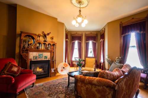 Cozy living room with a fireplace, elegant furniture, and warm lighting, featuring rich curtains and decorative accents.