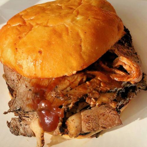 A close-up of a hearty sandwich filled with sliced beef and barbecue sauce, served on a golden bun.