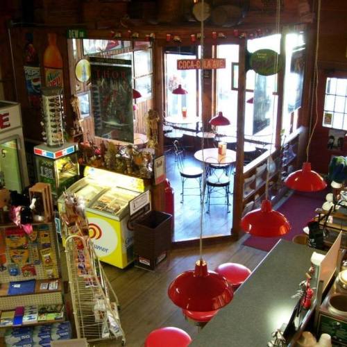 A cozy café interior with red pendant lights, tables, and a display of snacks and drinks.