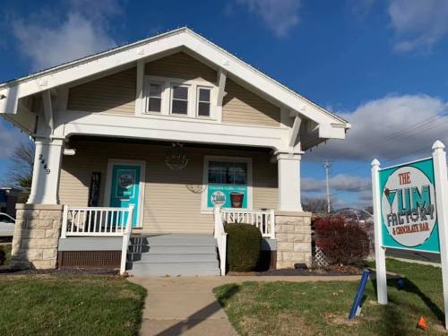A charming house with a sign for "The Yum Factory" and colorful doors, set against a blue sky.