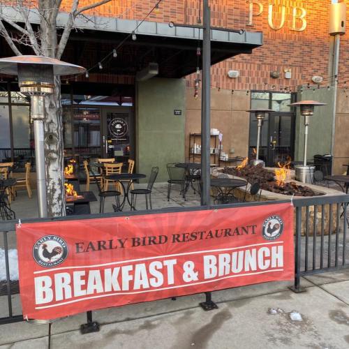 Outdoor seating area of Early Bird Restaurant with a banner promoting breakfast and brunch. Heaters are visible.