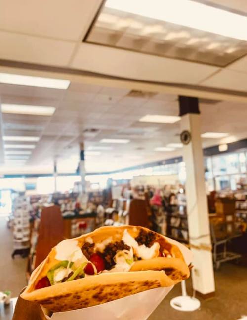 A close-up of a taco filled with meat, lettuce, and sour cream, with a bookstore in the background.