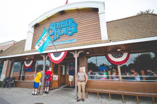 Exterior of a restaurant named "Summer House," featuring patriotic decorations and a man standing at the entrance.