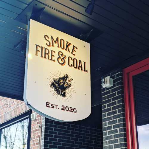 Sign for "Smoke Fire & Coal" featuring a bear graphic, established in 2020, mounted on a building exterior.