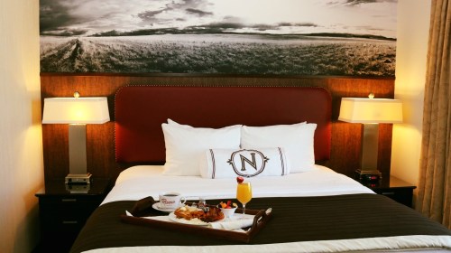 A cozy hotel room with a neatly made bed, two lamps, and a breakfast tray featuring food and a drink.