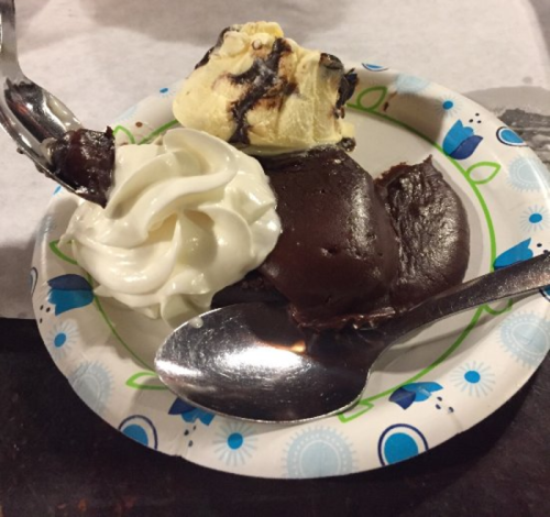 A plate with a serving of chocolate dessert, topped with whipped cream and a scoop of vanilla ice cream.