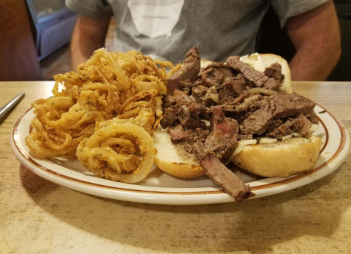 A plate with a sandwich filled with sliced beef and a side of crispy onion rings.