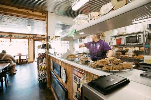 A cozy café interior with a counter displaying baked goods and a staff member serving customers.